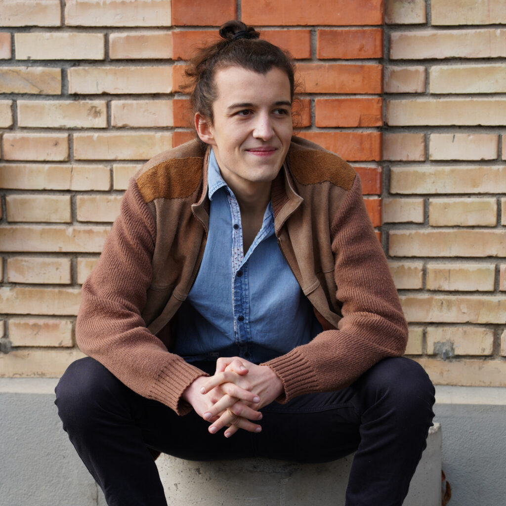 Media-Photo-10 Carlo Bechtel sitting in front of a brick wall looking to the right.