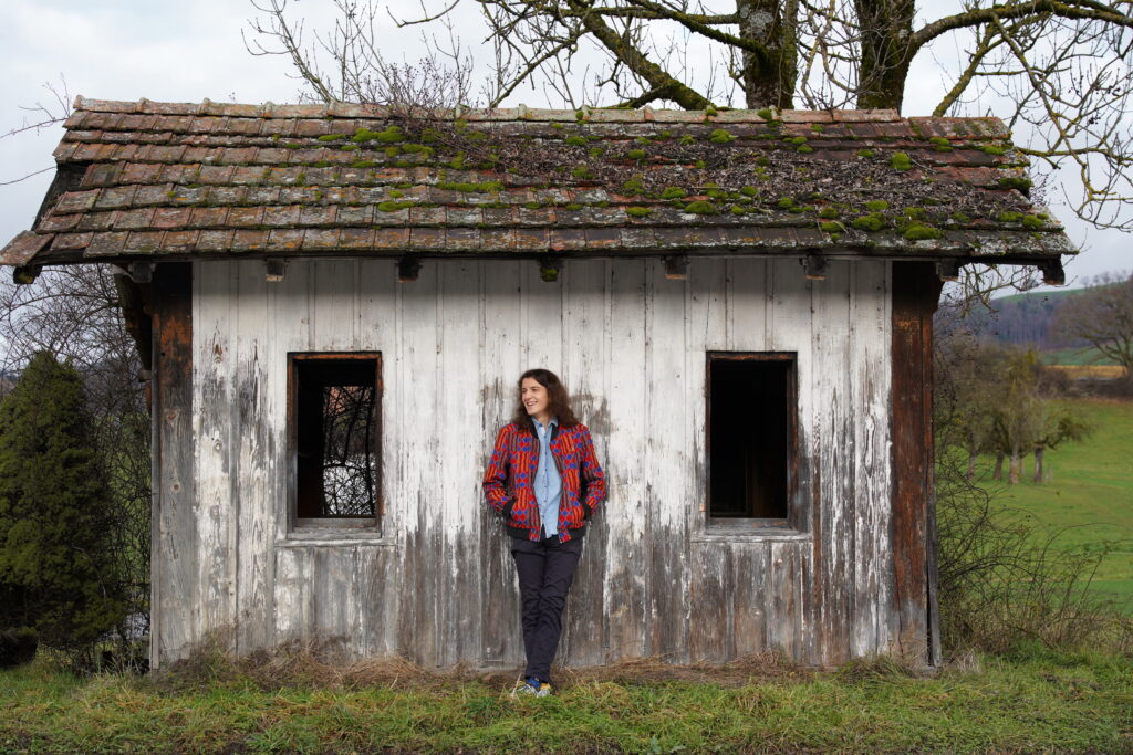 Media-Photo-11 Carlo Bechtel is leaning against an old wooden shack with two open windows and moss on top of the roof.