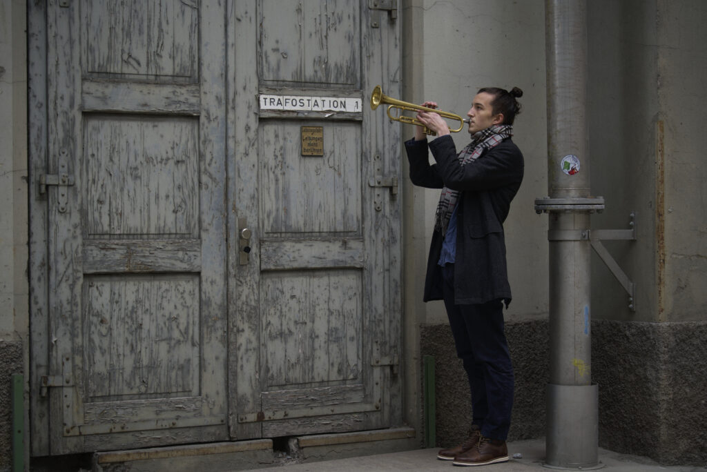Media-Photo-2 Carlo Bechtel standing next to an old door whilst playing on the trumpet.